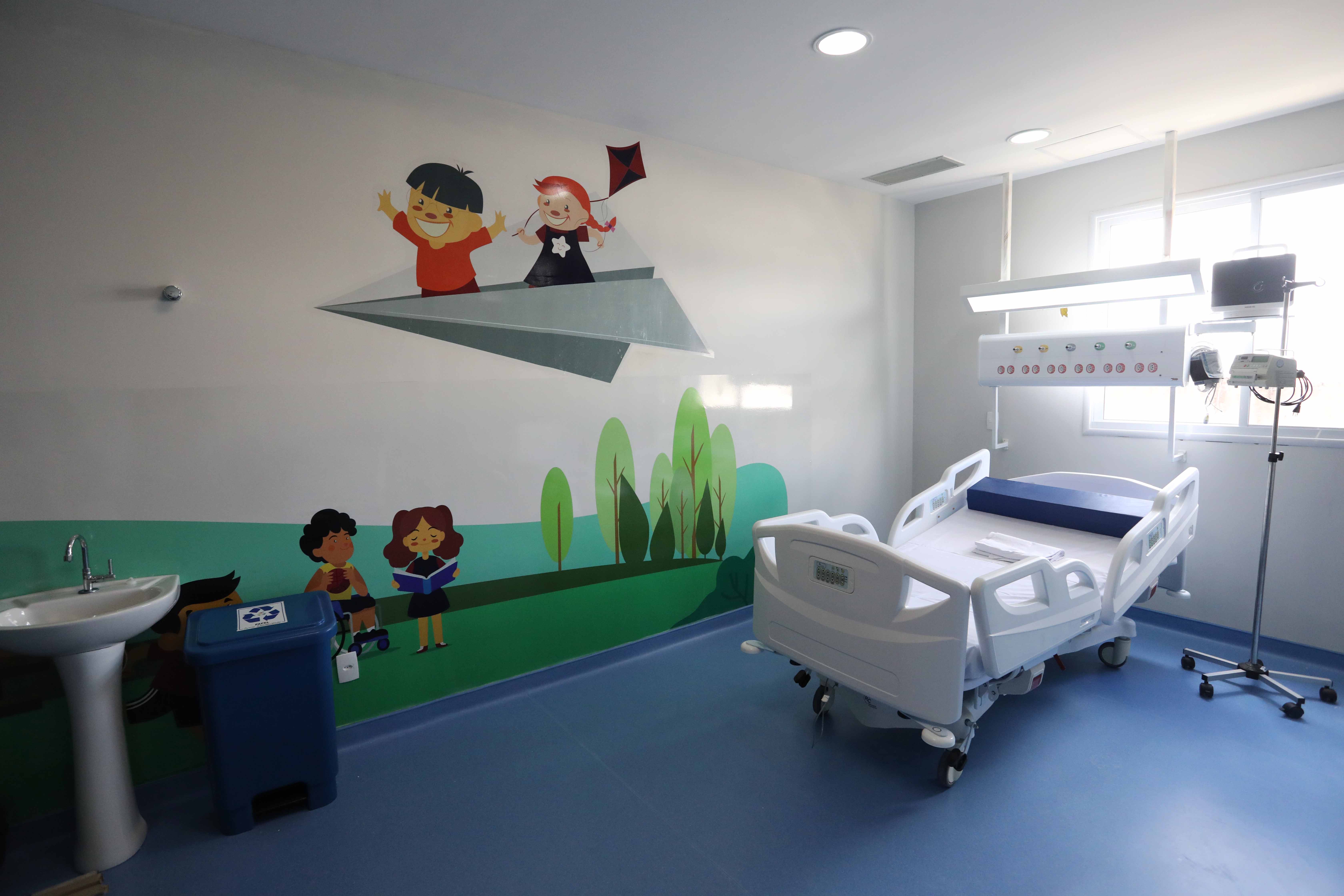 leito de hospital com parede ao fundo com desenhos infantis pintados nela